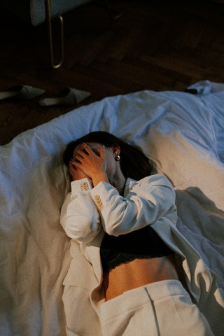 grieving woman lying on bed with hands over face